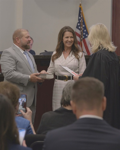 A couple stands before a judge in a courtroom during a formal ceremony with an American flag in the background.