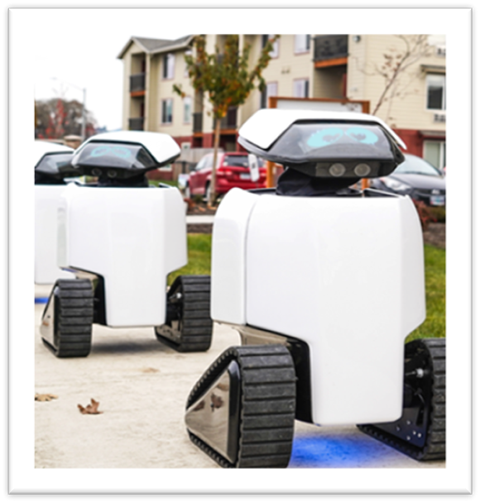 Three white autonomous delivery robots with tank-like tracks moving on a sidewalk in a residential neighborhood.