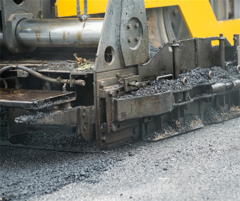 Close-up of asphalt paving machine spreading fresh black asphalt on a road surface during construction.